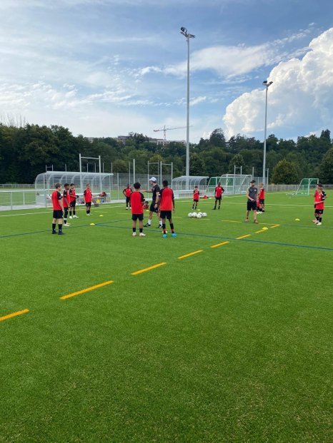 Séance d'entraînement FootEco à Genève : de jeunes footballeurs en maillots rouges perfectionnent leurs techniques sur terrain synthétique, encadrés par des coachs expérimentés.