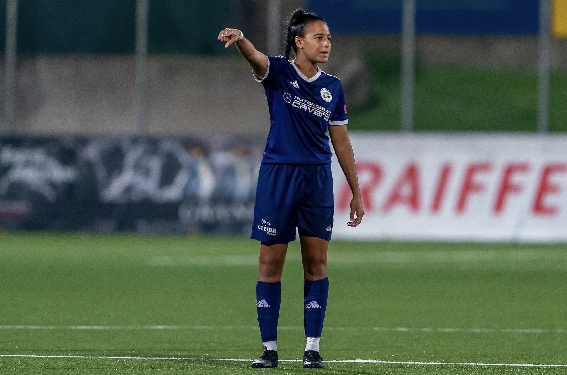 Leila Marrel, joueuse et entraîneure de football, en action sur le terrain, portant l'uniforme bleu de l'Étoile Carouge FC lors d'un match.