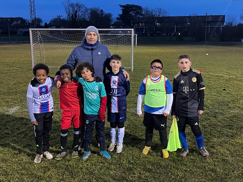 Un groupe de jeunes footballeurs pose aux côtés d’un scout expérimenté lors d’une séance d’entraînement en soirée. L’image reflète le travail de détection et d’accompagnement réalisé au sein du programme Footeco.